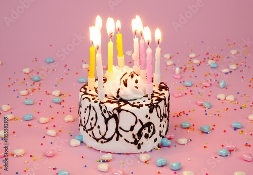 Birthday cake with burning candles on pink background with many colorful sprinkles. photo