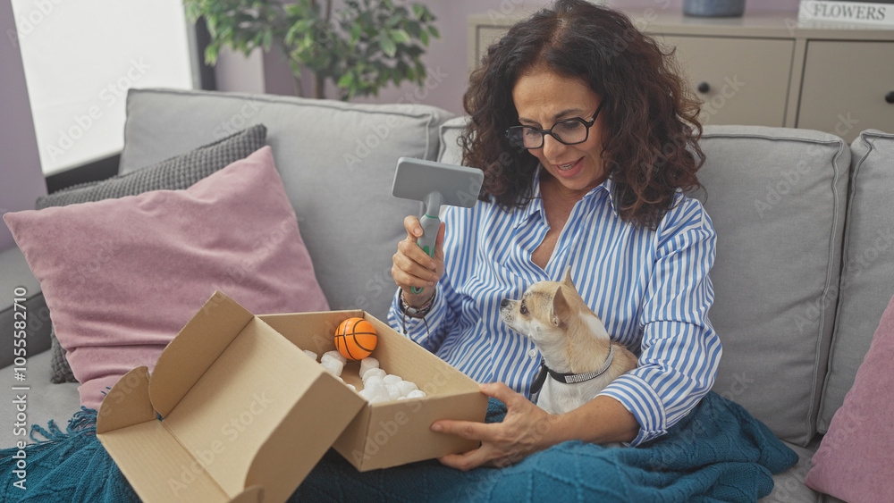 A middle-aged woman unboxing a toy basketball with her chihuahua on a cozy sofa indoors. A middle-aged woman unboxing a toy basketball with her chihuahua on a cozy sofa indoors.