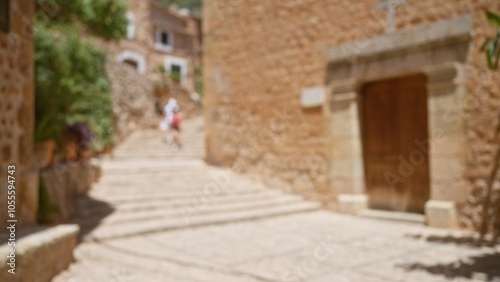 Outdoor scene in mallorca, showing blurred figures against ancient stone buildings and steps, highlights a sunlit mediterranean setting with defocused background and scenic architecture.