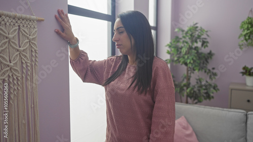 A contemplative woman stands indoors near a textured wall, embodying tranquility within a modern apartment. Free Download A contemplative woman stands indoors near a textured wall, embodying tranquility within a modern apartment. - GFXLoad