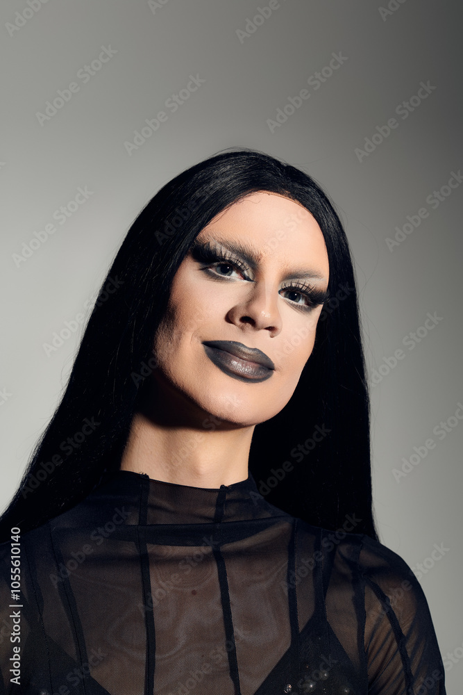 Naklejka premium A confident drag queen in a striking black outfit poses elegantly against a smooth grey backdrop.