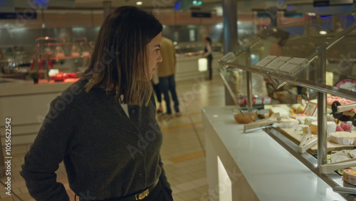 Woman browsing a buffet in a restaurant, showcasing various food options behind glass displays with an indoor, modern setting and casual attire.