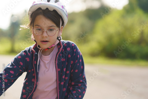 Little girl with glasses in helmet on the side of bike path. Concept of children's fun