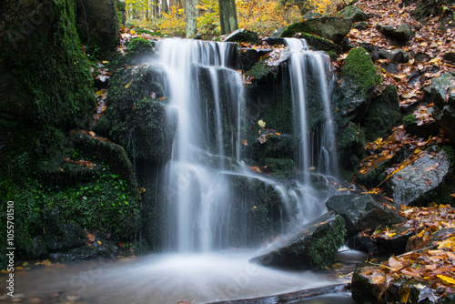 A forest stream with a waterfall in autumn, surrounded by vibrant colorful leaves.