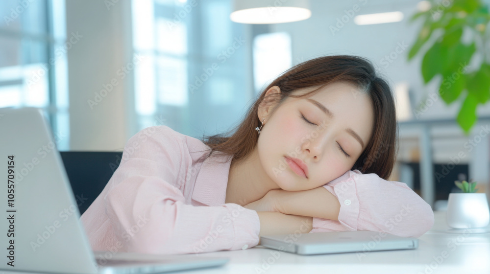 An Asian female employee is sleeping at her desk with a laptop in front of her. This image represents fatigue and exhaustion in the workplace. An Asian female employee is sleeping at her desk with a laptop in front of her. This image represents fatigue and exhaustion in the workplace.
