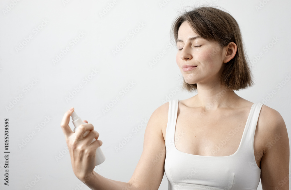 Girl applying moisturizing facial spray against white backdrop