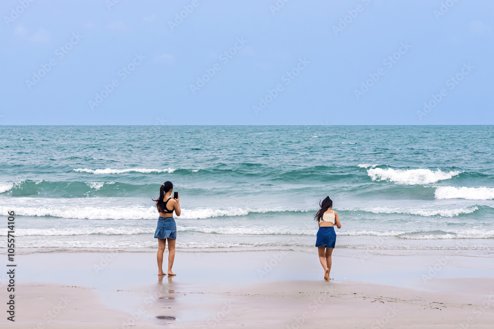 Back view of happy carefree woman using mobile phone at beach. Woman using smartphone standing at beach. Beautiful lovely young woman spending time at beach. Concept of travel, tourism and vacation. Back view of happy carefree woman using mobile phone at beach. Woman using smartphone standing at beach. Beautiful lovely young woman spending time at beach. Concept of travel, tourism and vacation.