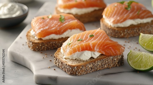 Whole grain bread sandwiches filled with cream cheese and smoked salmon presented on a marble board accompanied by lime wedges and sour cream