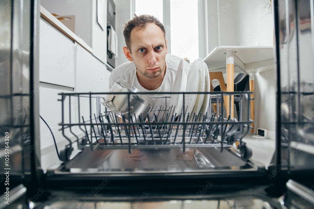 Surprised man holds his head after seeing a broken dishwasher