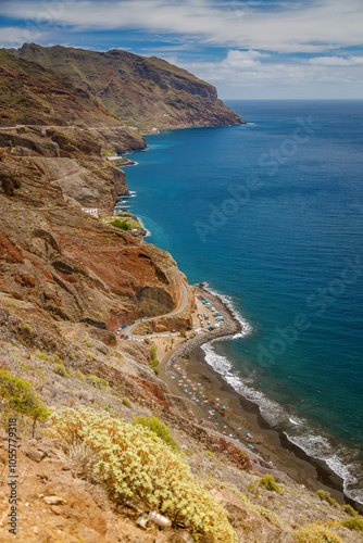 Rugged Playa de las Gaviotas in Tenerife with dark sand, steep cliffs, and a winding road leading to the beach