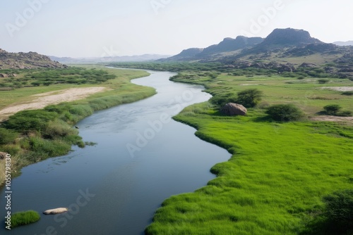 A river with a green grassy bank. The water is calm and clear. The landscape is peaceful and serene