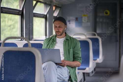 Thoughtful man passenger with laptop during electric train journey concentrating on tasks. Focused male freelancer in earphones remote works, productive use of travel time by railway public transport