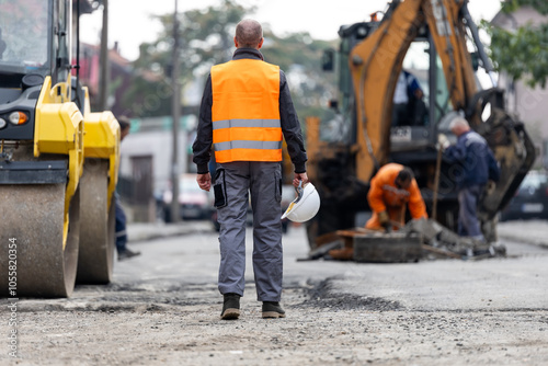 Fotografi Construction workers repair a road with heavy machinery in an urban environment