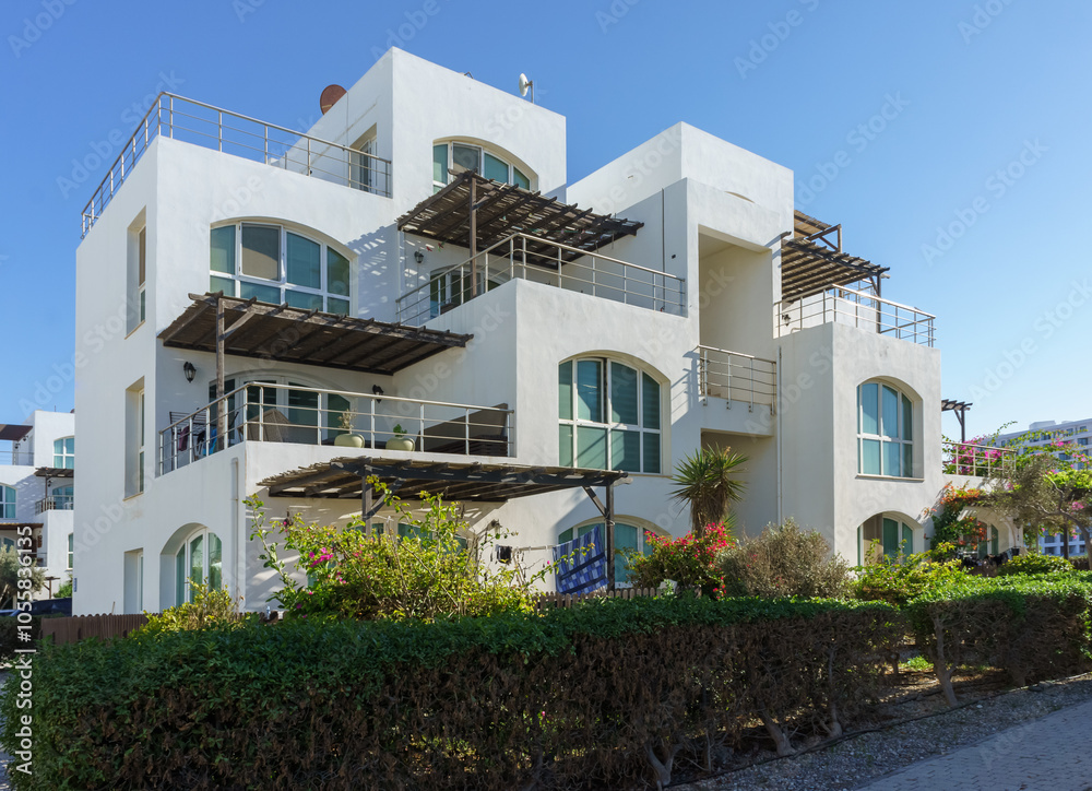 Obraz premium Charming coastal villa bathed in sunlight, surrounded by lush greenery in a vibrant neighborhood.