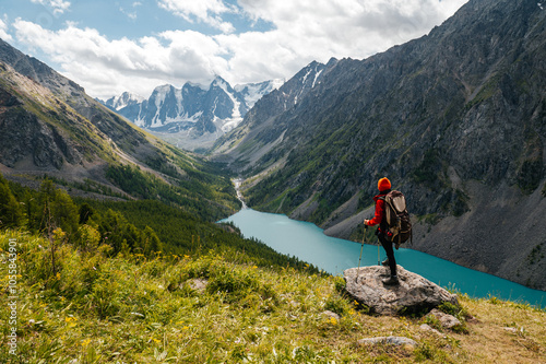 A tourist girl stands on a stone overlooking the beautiful mountains and Lake Shavlinskoye. Altai. Siberia