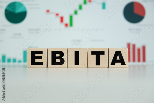 Wooden blocks spell out EBITA on a desk with financial charts in the soft-focus background photo