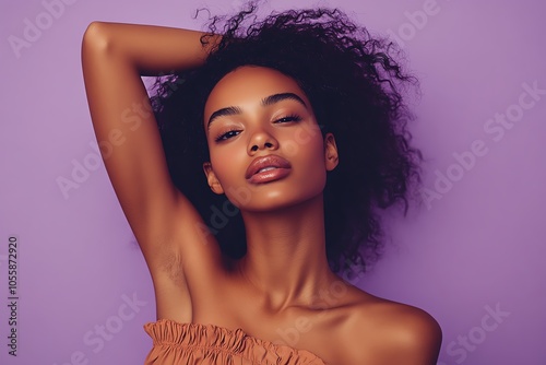 A chic African American woman in an off-shoulder top poses gracefully under studio lights, with a flat lavender background. photo