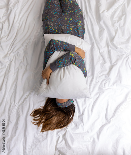 Person Lying on a Bed in Floral Pajamas Hugging a White Pillow with Hair Spread Out