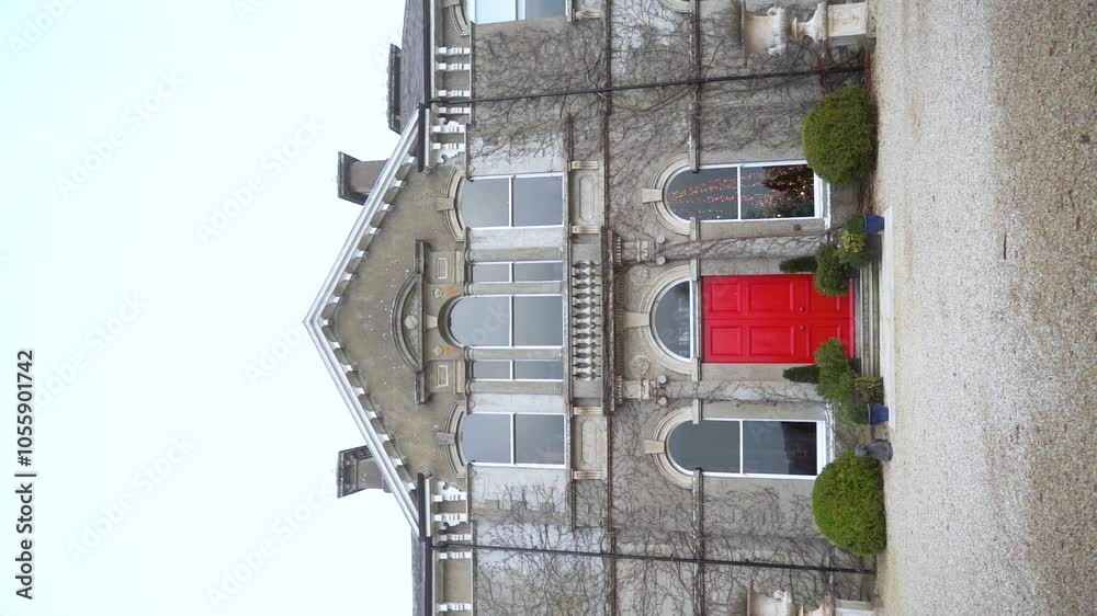 A majestic stone building with a red door, surrounded by ivy A majestic stone building with a red door, surrounded by ivy
