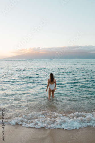 A peaceful scene of a woman stepping into the ocean as the sun sets, creating a magical, reflective moment by the sea.