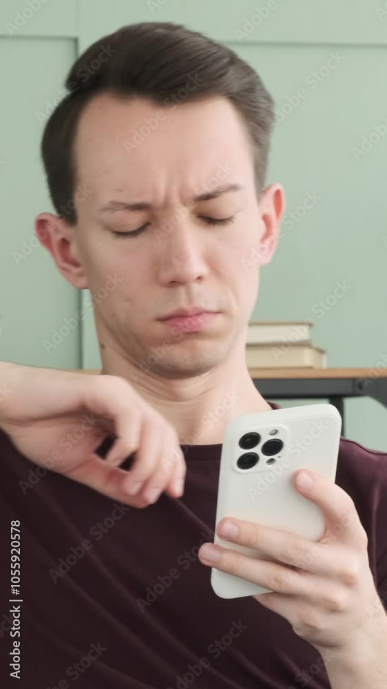 Serious young adult Caucasian man using mobile phone for online texting or internet browsing, resting on sofa at home. Vertical video. Serious young adult Caucasian man using mobile phone for online texting or internet browsing, resting on sofa at home. Vertical video.