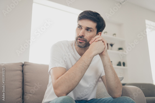 Thoughtful man relaxing on the sofa at home in bright daylight, enjoying a peaceful weekend indoors