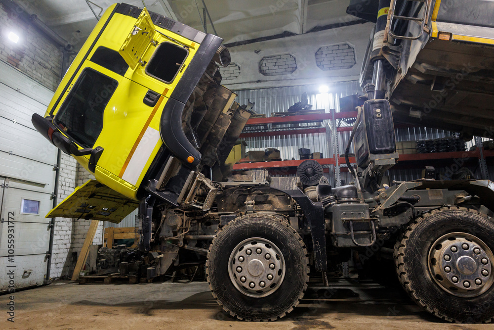 Obraz premium Inside a spacious garage, a bright yellow dump truck is currently undergoing repairs and maintenance to ensure it functions properly again