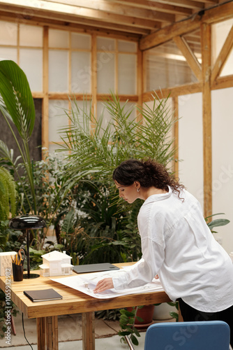 Architect examining large paper documents on wooden desk surrounded by lush green plants photo