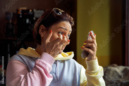 Woman applying makeup with hand mirror in cozy cafe setting