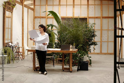 Architect reading documents while standing in modern office space with plants and wooden features photo