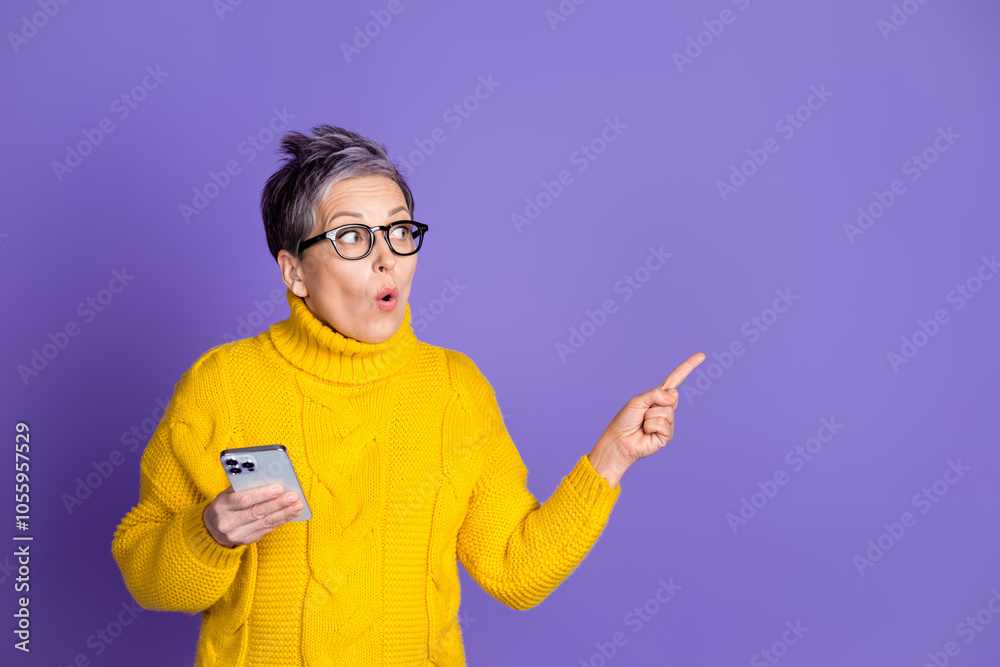 Photo of shiny impressed lady dressed yellow pullover chatting modern gadget pointing empty space isolated purple color background Photo of shiny impressed lady dressed yellow pullover chatting modern gadget pointing empty space isolated purple color background