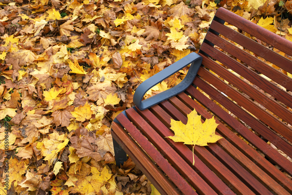 One yellow maple leaf lies on brown wooden bench in autumn park. Fallen colorful leaves blurred on background with copy space. Fall mood concept.