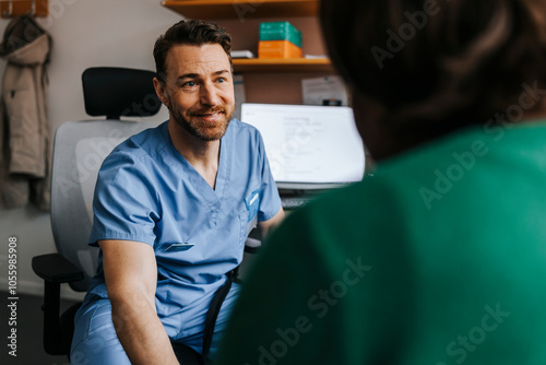 Smiling medical professional in scrubs consoling patient while sitting on chair in examination room