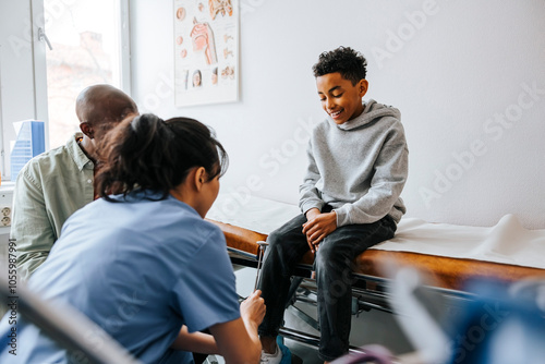 Female pediatrician checking knee of boy with reflex hammer in medical examination room photo