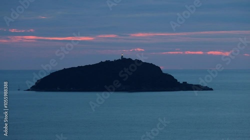 Blinking lighthouse on an island in the sea at sunset