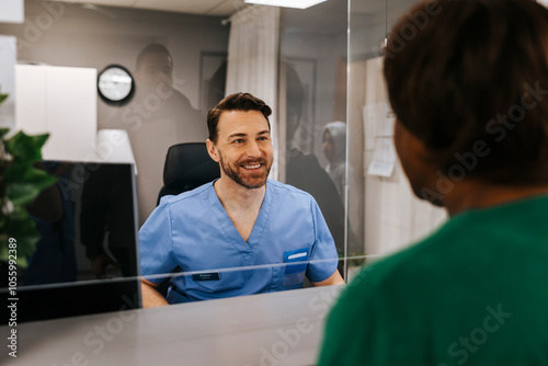 Happy male receptionist seen through glass assisting patient standing at medical clinic