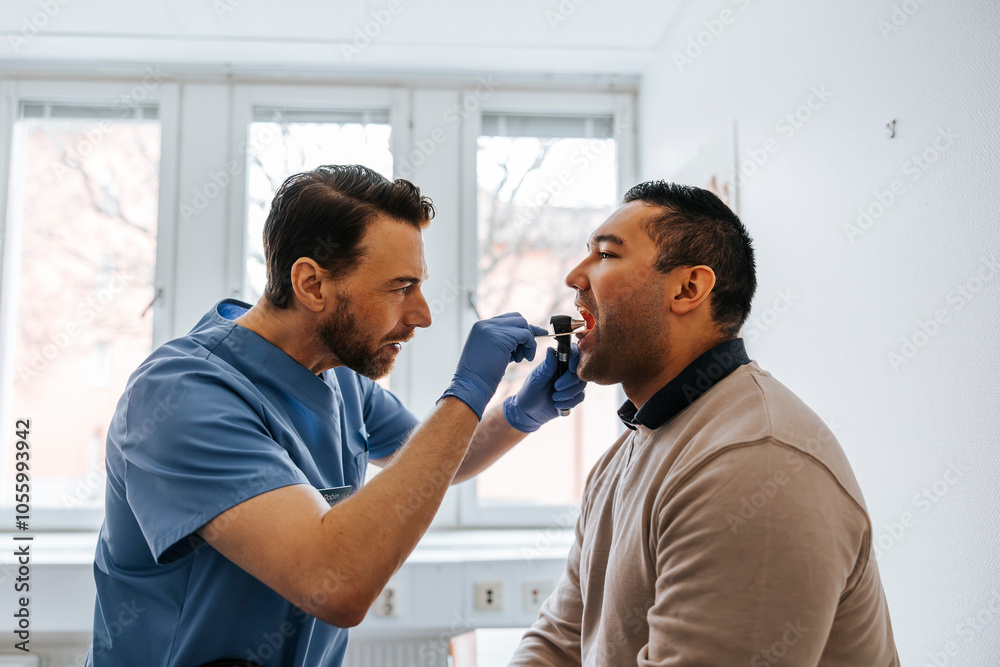 Male medical expert examining throat of man using tongue depressor in examination room at hospital