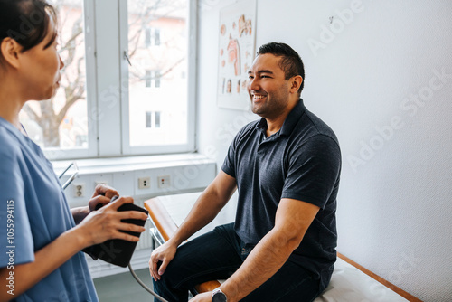 Happy man sitting on examination table and talking with female doctor in medical room at hospital photo