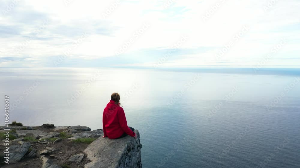 Girl in red jacket sitting on top of mountain with beautiful view of norwegian sea, Ryten, Lofoten islands Girl in red jacket sitting on top of mountain with beautiful view of norwegian sea, Ryten, Lofoten islands