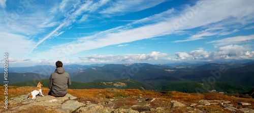 man and dog sitting on top of mountain contemplating meditation nature. Horizontal long banner. Hiking with pet