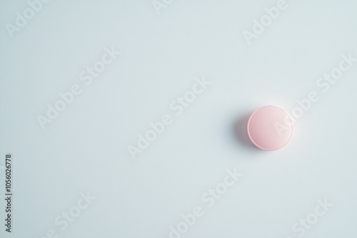 Single pink round pill on light blue background. Top view medical composition with copy space.