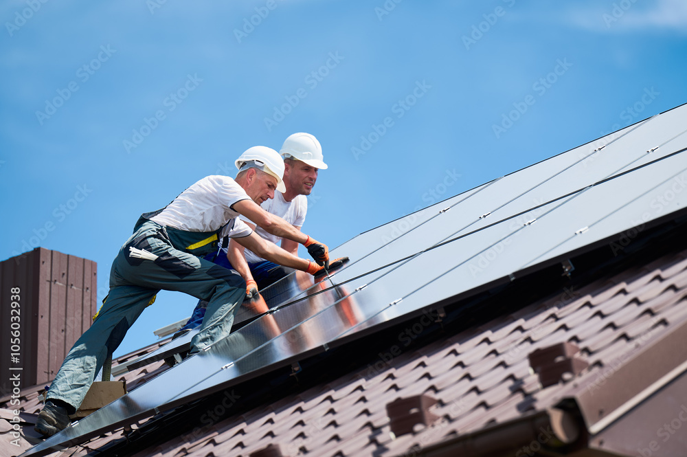 Workers building photovoltaic solar panel system on rooftop of house. Technicians in helmets installing solar module with help of hex key outdoors. Alternative and renewable energy generation concept. Workers building photovoltaic solar panel system on rooftop of house. Technicians in helmets installing solar module with help of hex key outdoors. Alternative and renewable energy generation concept.