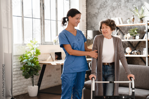 Patient in pain. Medical worker caretaker nurse supporting helping aiding senior woman grandmother with walking frame after injury trauma in hospice