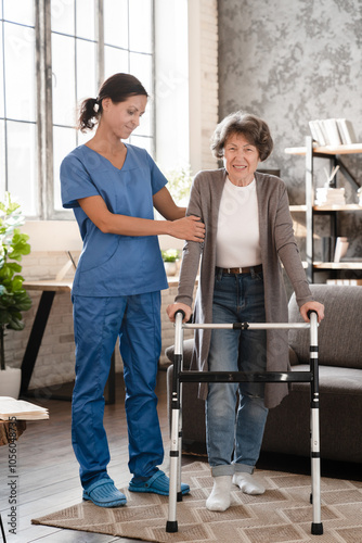 Vertical shot of nurse medical staff worker helping assisting aiding senior old elderly handicapped disabled immobilized woman patient with walking frame feeling pain after injury