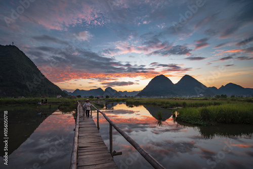 A middle-aged woman was riding her bicycle across a wooden bridge in Bac Son Village. Beautiful sunset in the evening