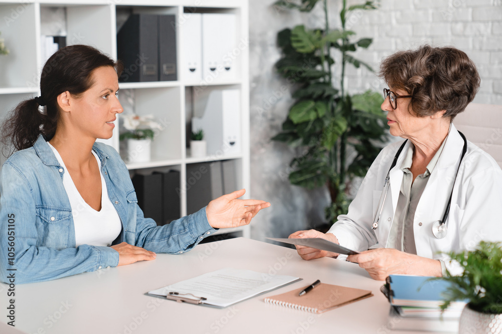 Female middle-aged patient complaining about illness diseases symptoms to elderly senior doctor general practitioner gynecologist in hospital Female middle-aged patient complaining about illness diseases symptoms to elderly senior doctor general practitioner gynecologist in hospital