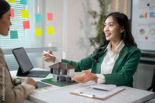A woman in a green jacket is talking to another woman at a desk