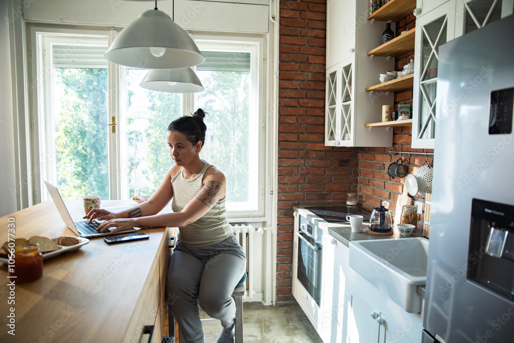 Focused woman working on laptop in cozy kitchen with morning light Focused woman working on laptop in cozy kitchen with morning light