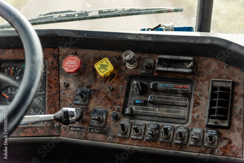 Interior View of an Old Semi Truck Dashboard: Dusty Controls for Air Brakes, Cruise Control, and Climate Control with a Classic Wood Grain Finish, Featuring Keys in the Ignition, switches and sliders photo