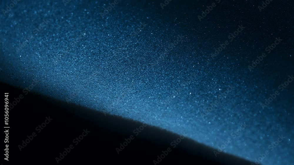 Blue light shining on dust particles falling in slow motion. Abstract macro shot. 